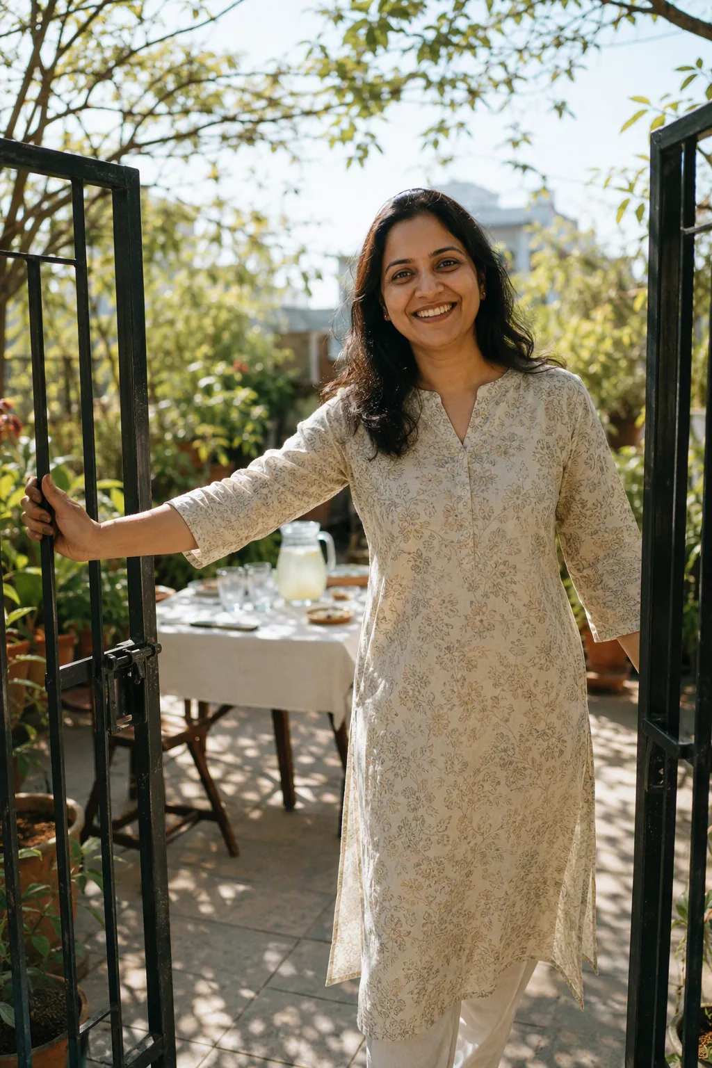 A woman welcoming guests through the gate of her sunlit terrace garden